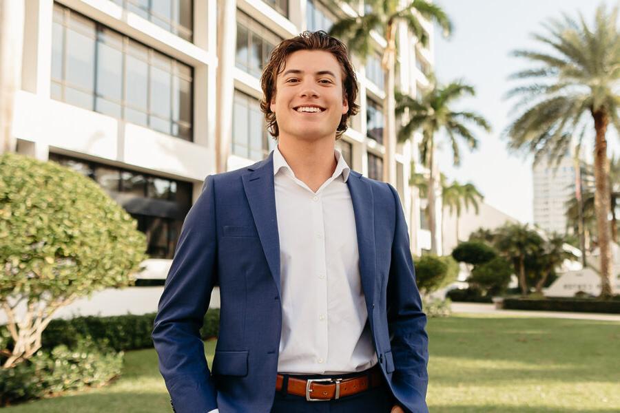 a male student standing outside of a building on campus at Palm Beach Atlantic University